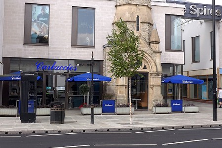 cafe with outdoor seating, blue parasols and the remains of part of a church spire