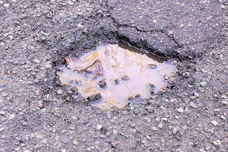 Close up of a small but deep pothole with muddy water in a tarmac road