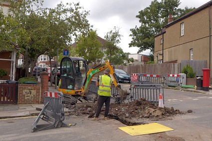 small digger working on a narrow trench across a road