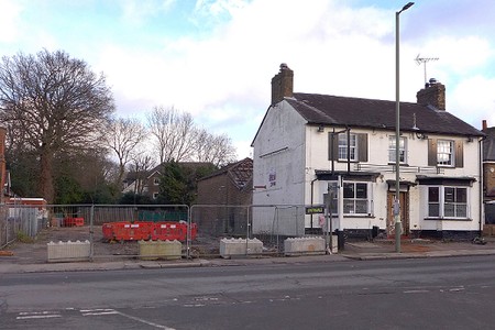 White painted closed pub with cleared building site fenced off